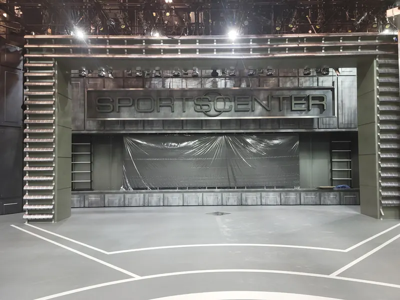 Gray studio floor with white line work in front of a sports broadcast set
