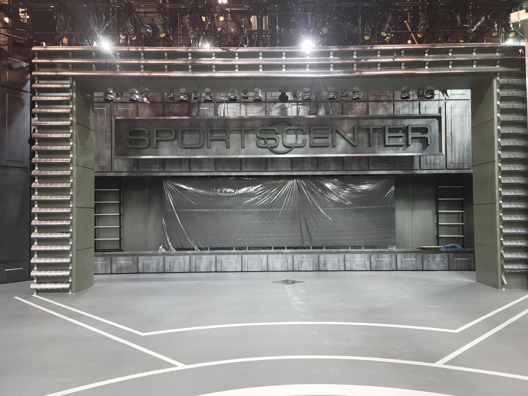 Gray studio floor with white line work in front of a sports broadcast set