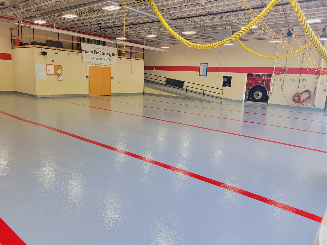 Wide view of the firehouse apparatus bay floor with a fire truck parked at the far side